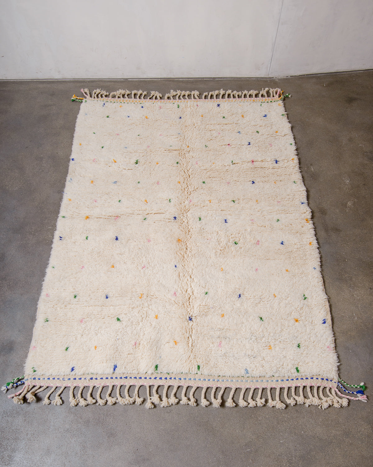 Berberlin Beniourain rug in cream wool with coloured dots laying on concrete floor.